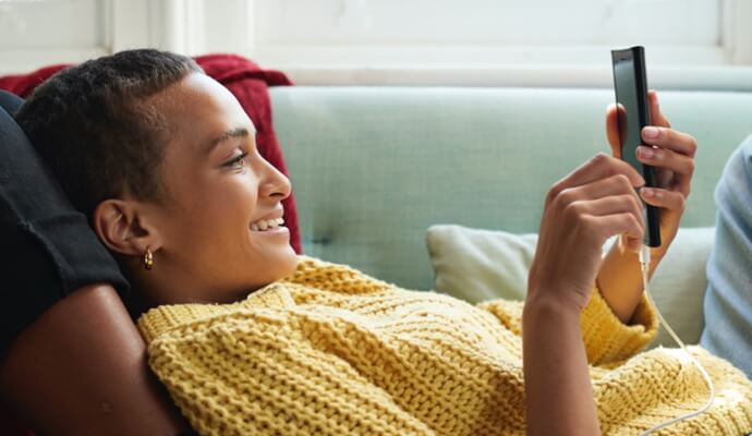 nainen sohvalla katsomassa kännykkää ja käynnistämässä Norton 360 AntiVirus Plus -ohjelmaa.