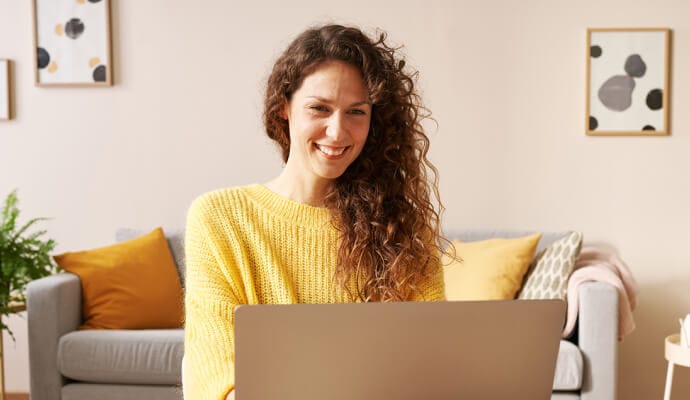 Kannettavaa tietokonetta käyttävä nainen hymyilee ja käynnistää Norton Safe Searchin.